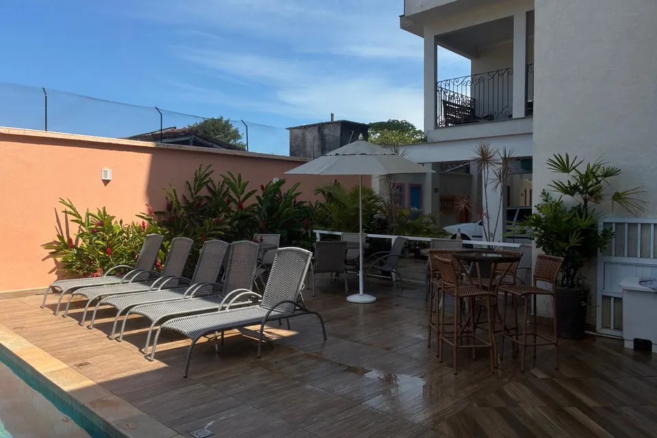 Espreguiçadeiras, guarda-sol e mesas altas na área da piscina do Villa Bela